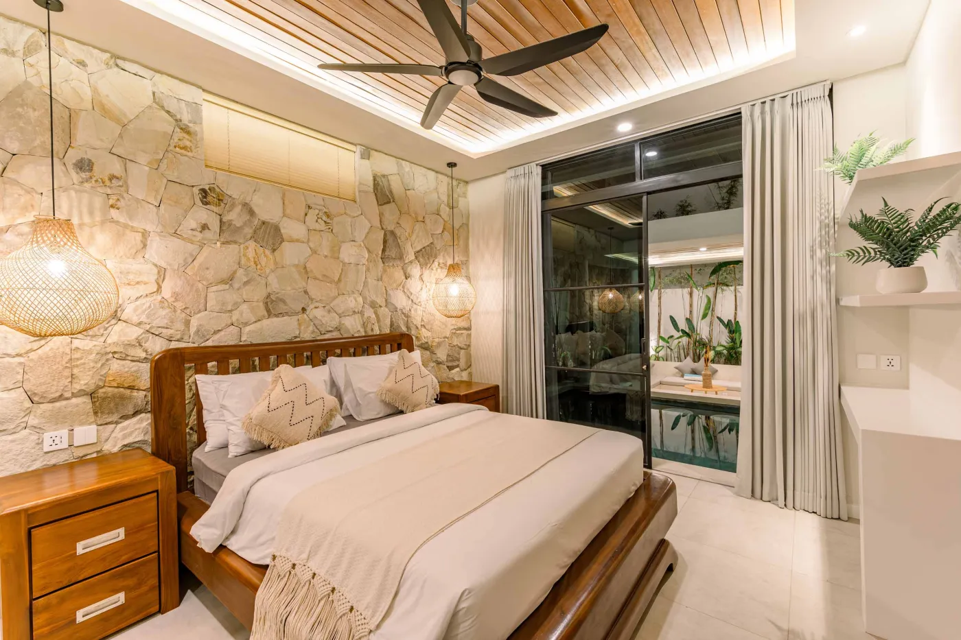 Luxurious modern bathroom featuring a white freestanding bathtub filled with water and red rose petals, adjacent glass shower, large window, and potted plant. - Bali Villas