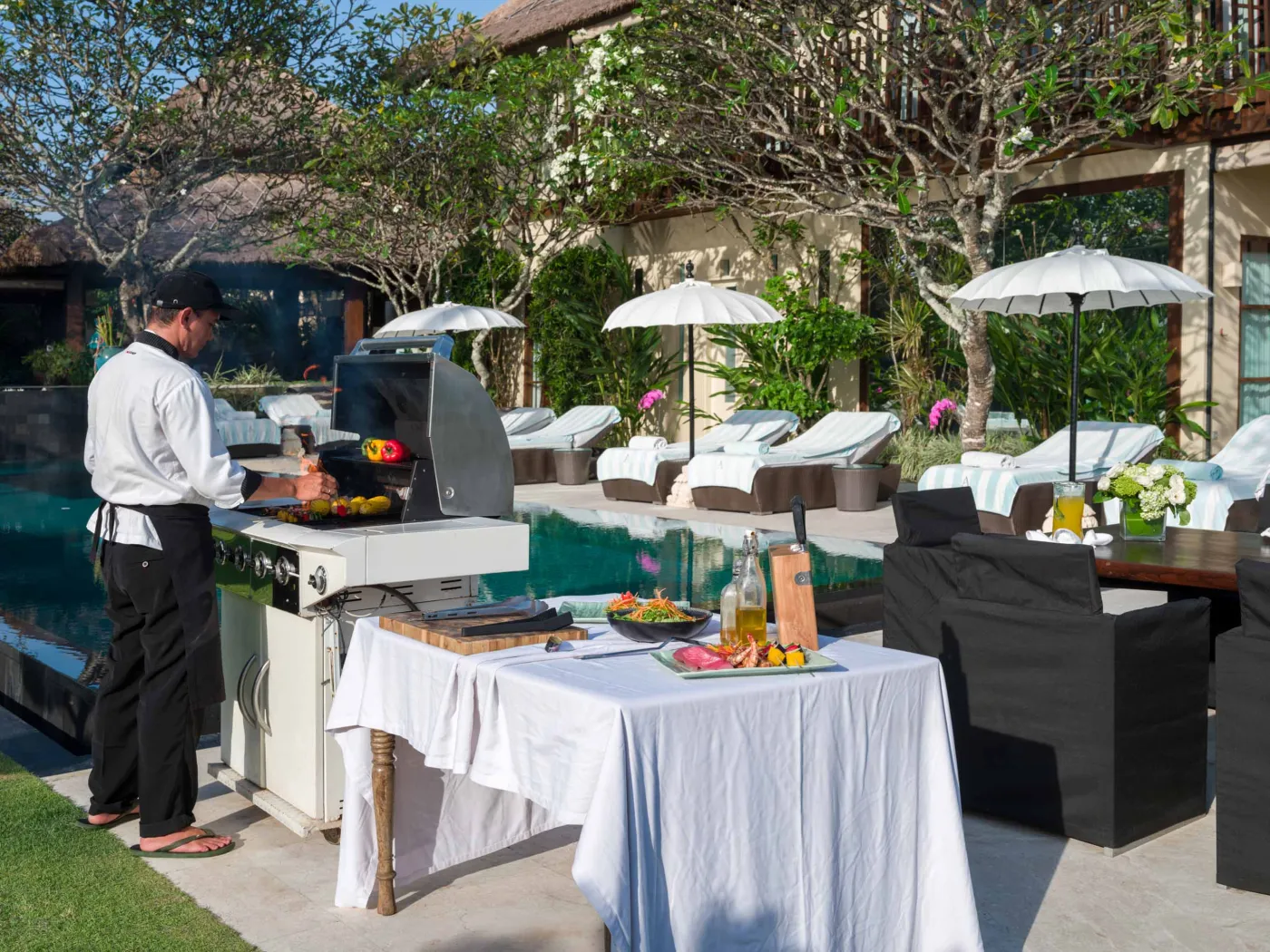 Curved stone terrace with white cushioned lounge overlooking Bali beach, ocean, and tropical gardens. - Bali Villas