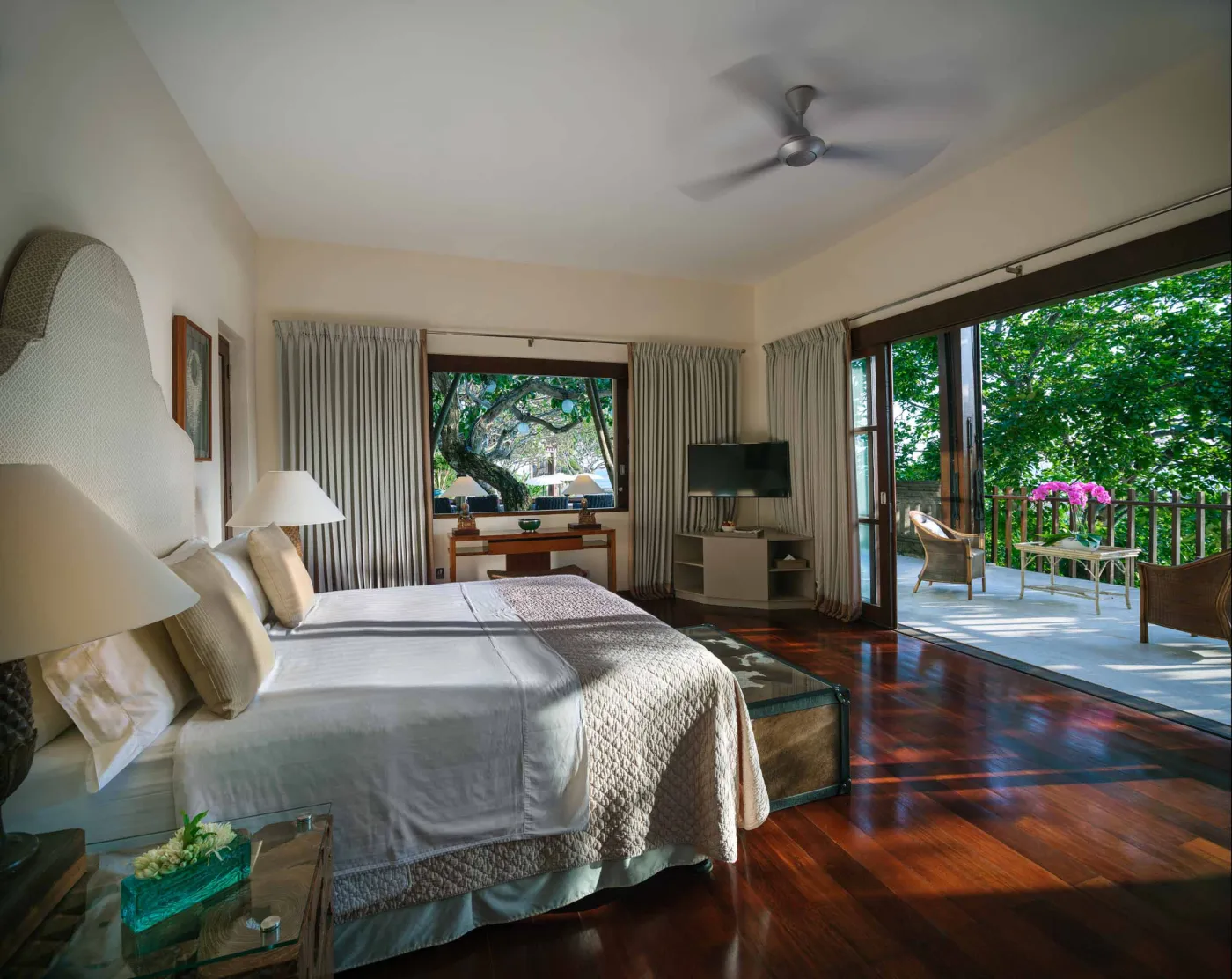 Curved stone terrace with white cushioned lounge overlooking Bali beach, ocean, and tropical gardens. - Bali Villas