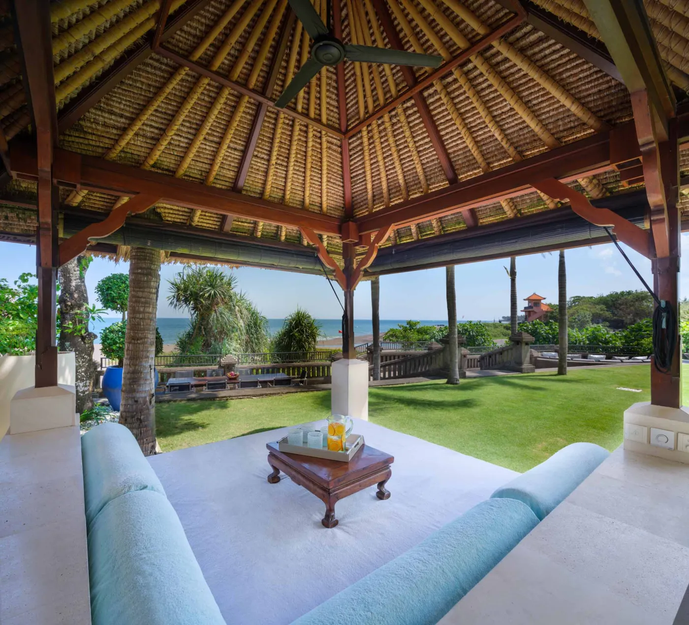 Curved stone terrace with white cushioned lounge overlooking Bali beach, ocean, and tropical gardens. - Bali Villas