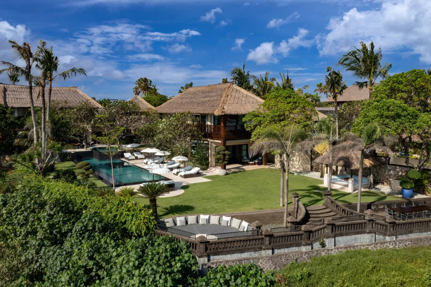 Curved stone terrace with white cushioned lounge overlooking Bali beach, ocean, and tropical gardens. - Bali Villas