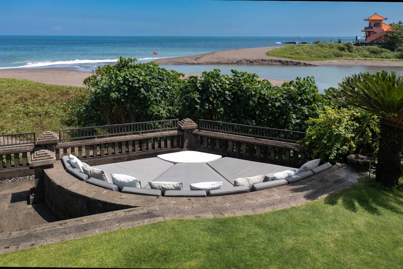 Curved stone terrace with white cushioned lounge overlooking Bali beach, ocean, and tropical gardens. - Bali Villas