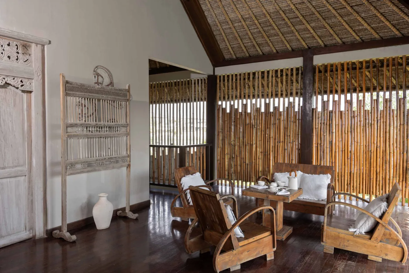 Spacious Balinese pavilion interior with thatched roof, white modular sofas, woven accents, and lush garden view through open wooden frames. - Bali Villas