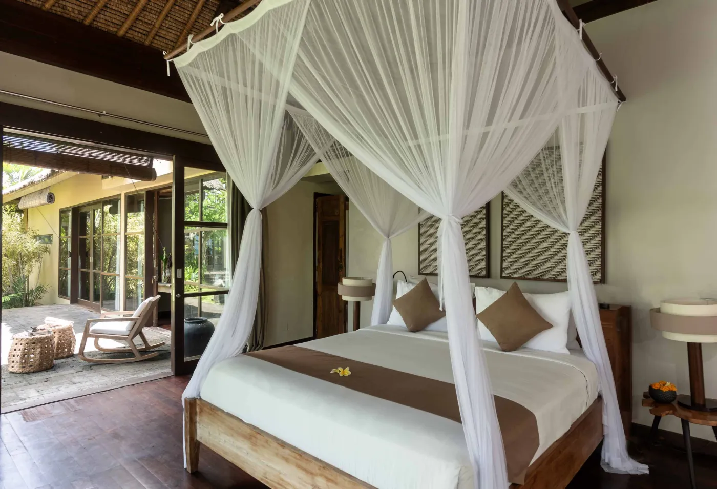 Spacious Balinese pavilion interior with thatched roof, white modular sofas, woven accents, and lush garden view through open wooden frames. - Bali Villas