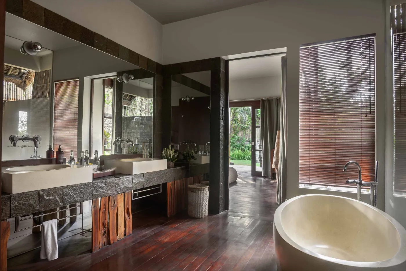 Spacious Balinese pavilion interior with thatched roof, white modular sofas, woven accents, and lush garden view through open wooden frames. - Bali Villas