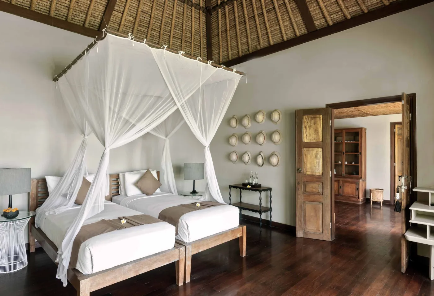 Spacious Balinese pavilion interior with thatched roof, white modular sofas, woven accents, and lush garden view through open wooden frames. - Bali Villas