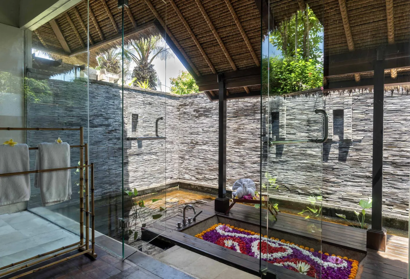 Spacious Balinese pavilion interior with thatched roof, white modular sofas, woven accents, and lush garden view through open wooden frames. - Bali Villas