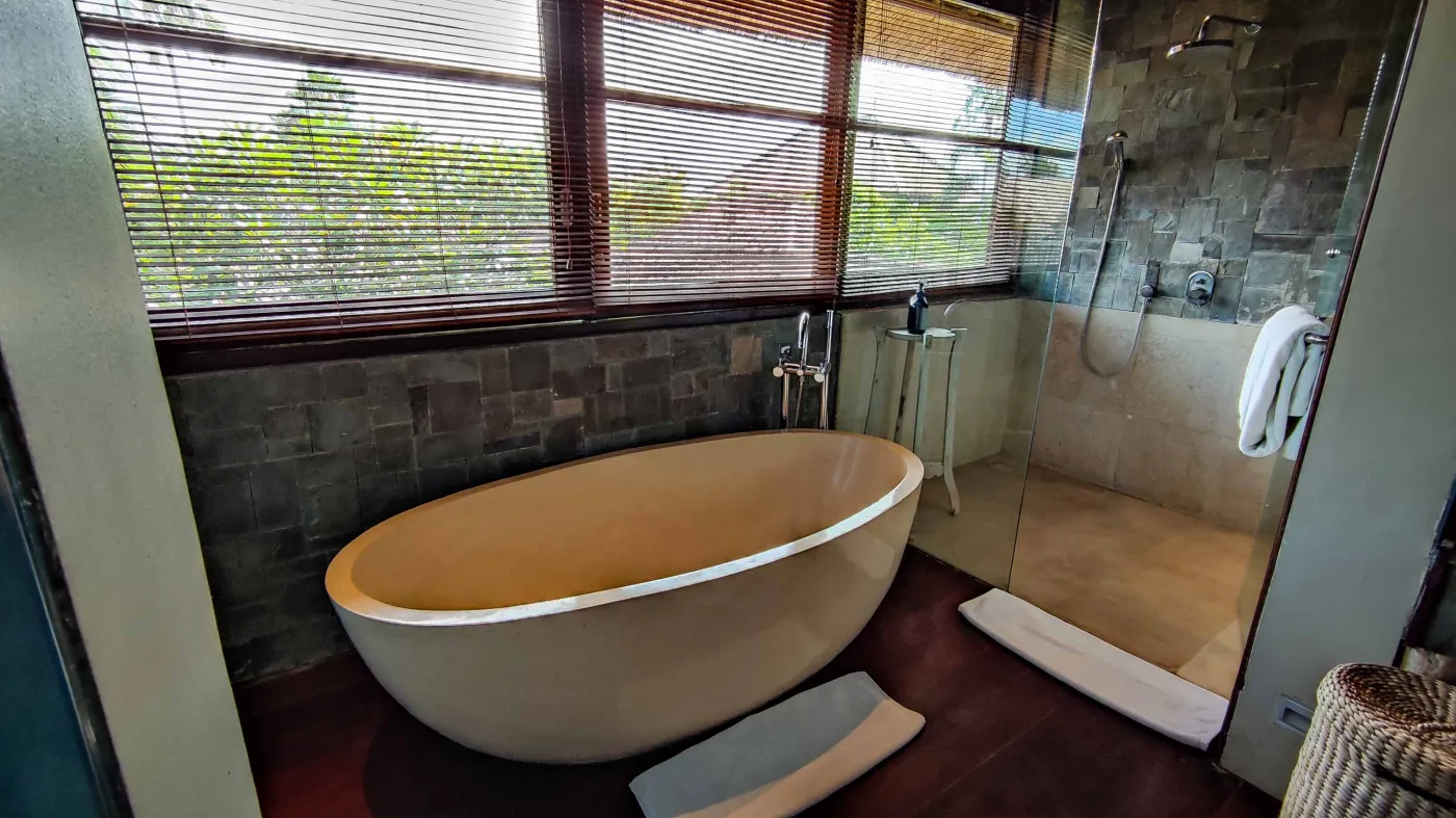 Luxury infinity pool at Bali beach resort, with loungers, umbrellas, tropical trees, and ocean view. - Bali Villas