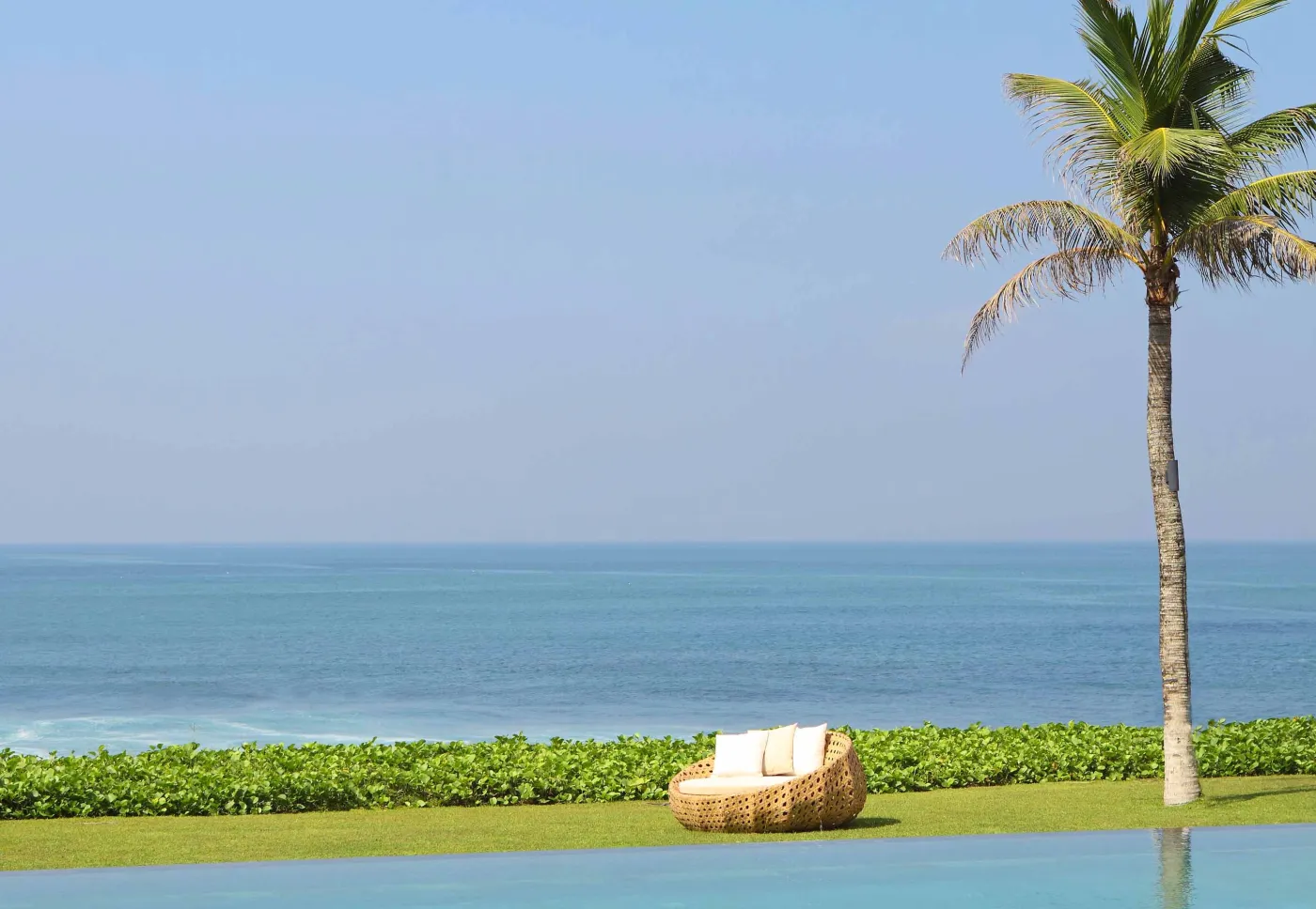 Luxury infinity pool at Bali beach resort, with loungers, umbrellas, tropical trees, and ocean view. - Bali Villas