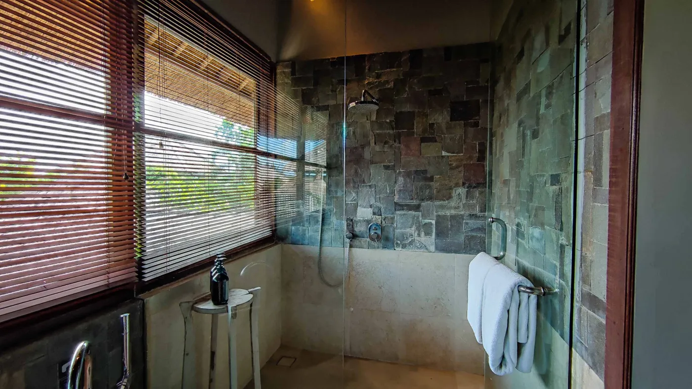 Luxury infinity pool at Bali beach resort, with loungers, umbrellas, tropical trees, and ocean view. - Bali Villas