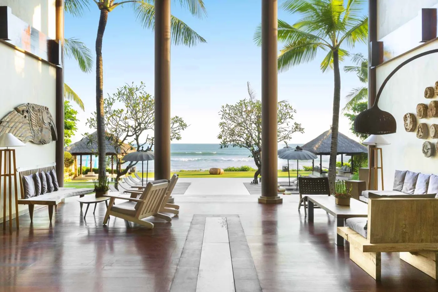 Luxury infinity pool at Bali beach resort, with loungers, umbrellas, tropical trees, and ocean view. - Bali Villas