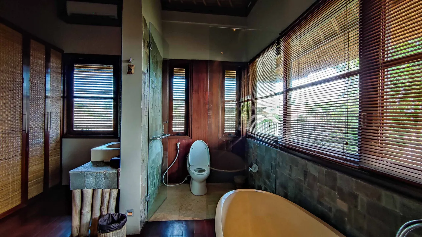 Luxury infinity pool at Bali beach resort, with loungers, umbrellas, tropical trees, and ocean view. - Bali Villas