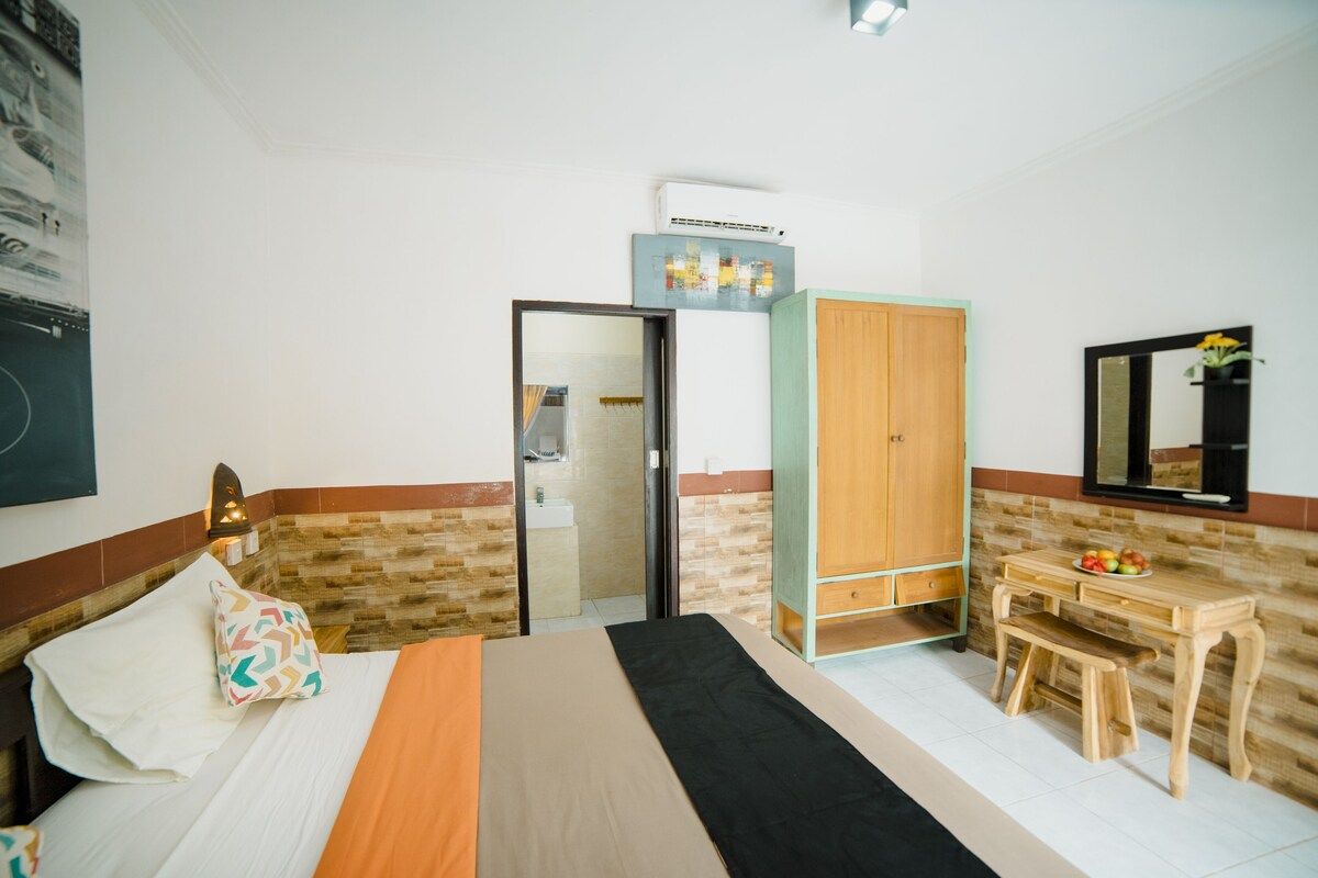Cozy tropical bedroom with a wooden double bed, orange sheets, patterned pillows, abstract black-and-white wall art, and ornate wall sconces. - Bali Villas