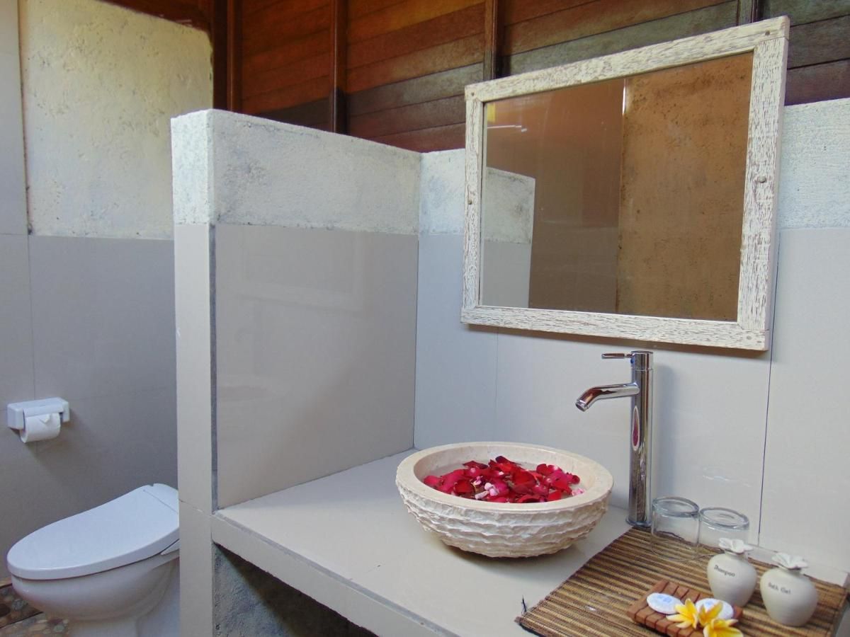 Rustic tropical bathroom with wooden walls, pebble tile floor, woven sink basin, and open shower. - Bali Villas