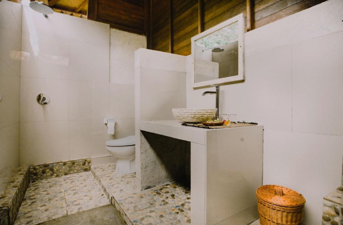 Rustic tropical bathroom with wooden walls, pebble tile floor, woven sink basin, and open shower. - Bali Villas