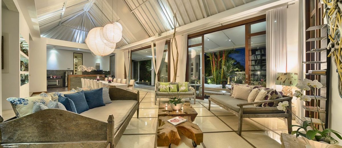 Luxurious spa bathroom with a freestanding tub filled with red rose petals and floating candles, orchids, white towels, and bamboo-shaded tropical window. - Bali Villas