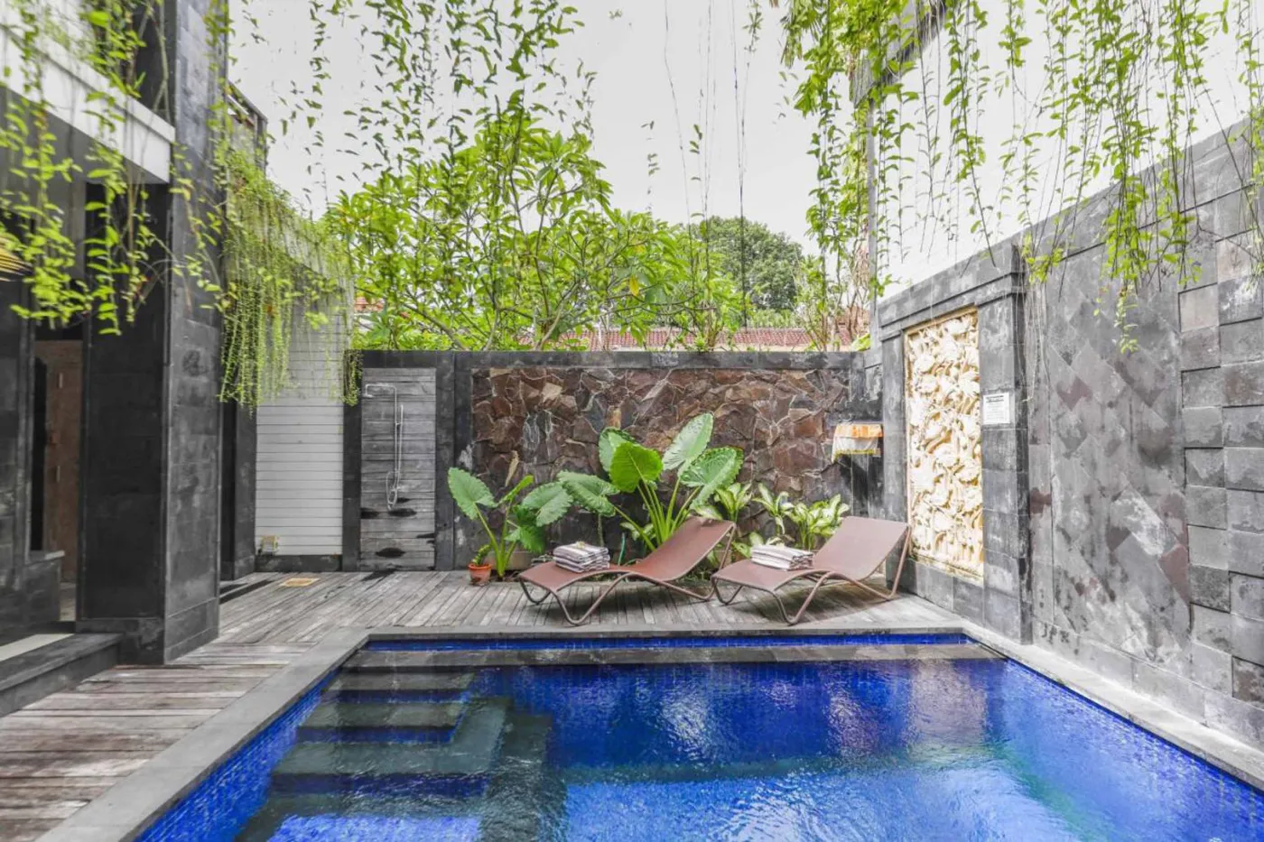 Modern bathroom with wooden bowl sink on black vanity, white toilet, glass shower enclosure, and neutral tiled walls. - Bali Villas