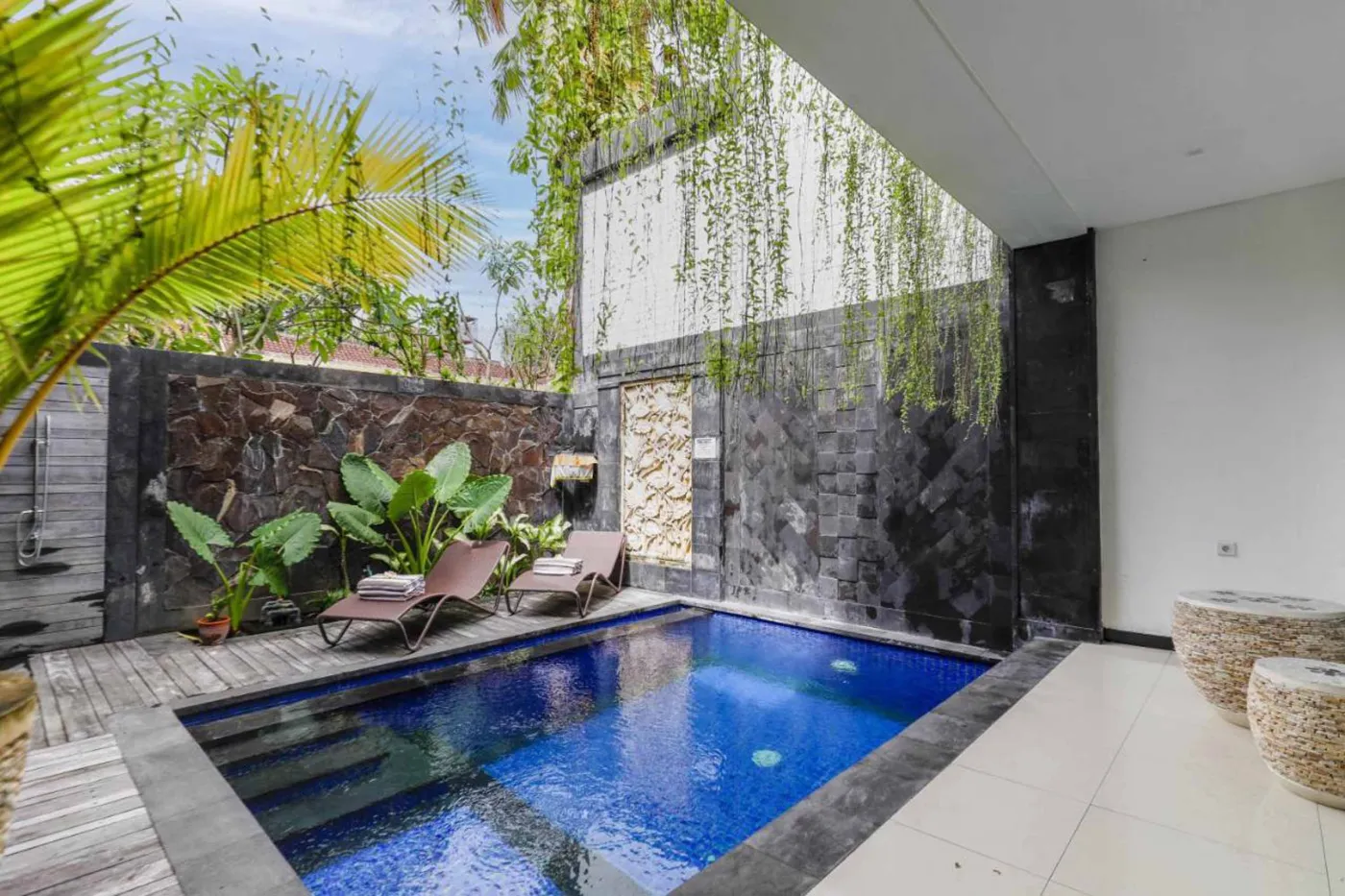 Modern bathroom with wooden bowl sink on black vanity, white toilet, glass shower enclosure, and neutral tiled walls. - Bali Villas