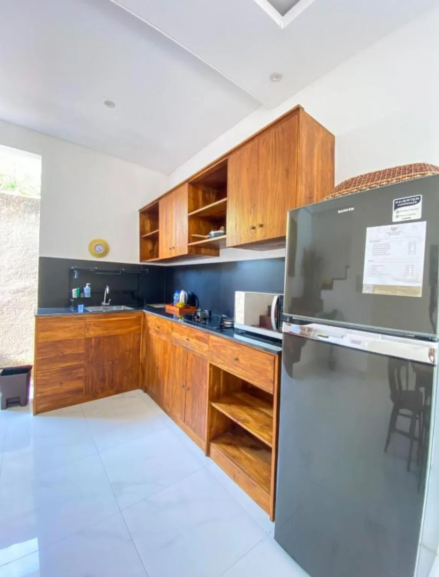 Cozy Balinese villa dining area with wooden table and chairs, kitchenette, framed Hindu deity artwork, and modern LED lighting. - Bali Villas
