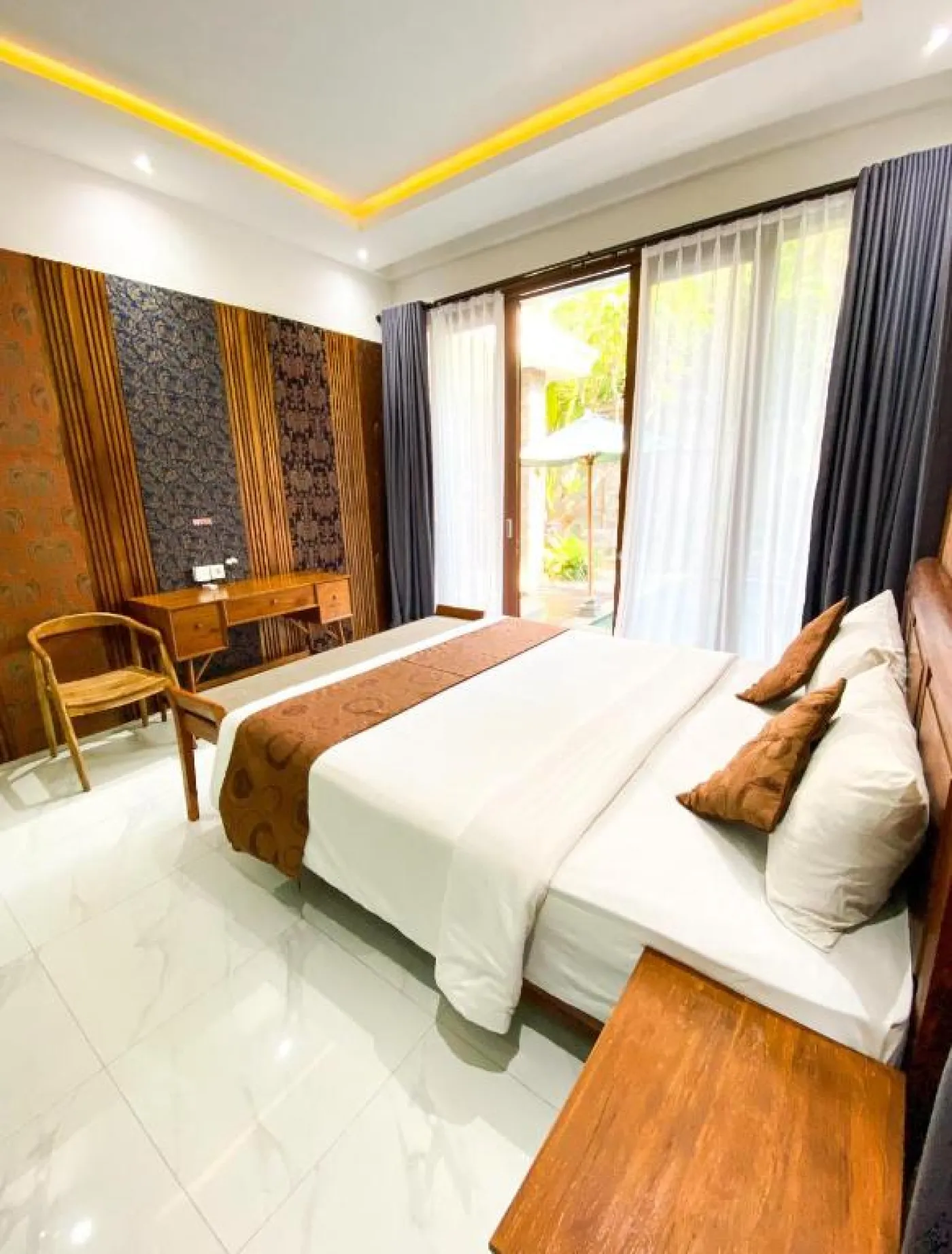 Cozy Balinese villa dining area with wooden table and chairs, kitchenette, framed Hindu deity artwork, and modern LED lighting. - Bali Villas