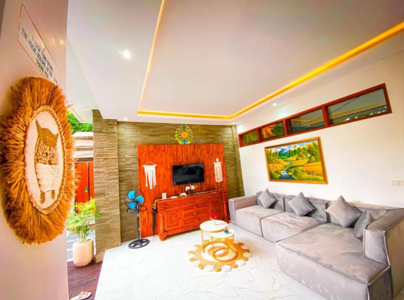 Cozy Balinese villa dining area with wooden table and chairs, kitchenette, framed Hindu deity artwork, and modern LED lighting. - Bali Villas