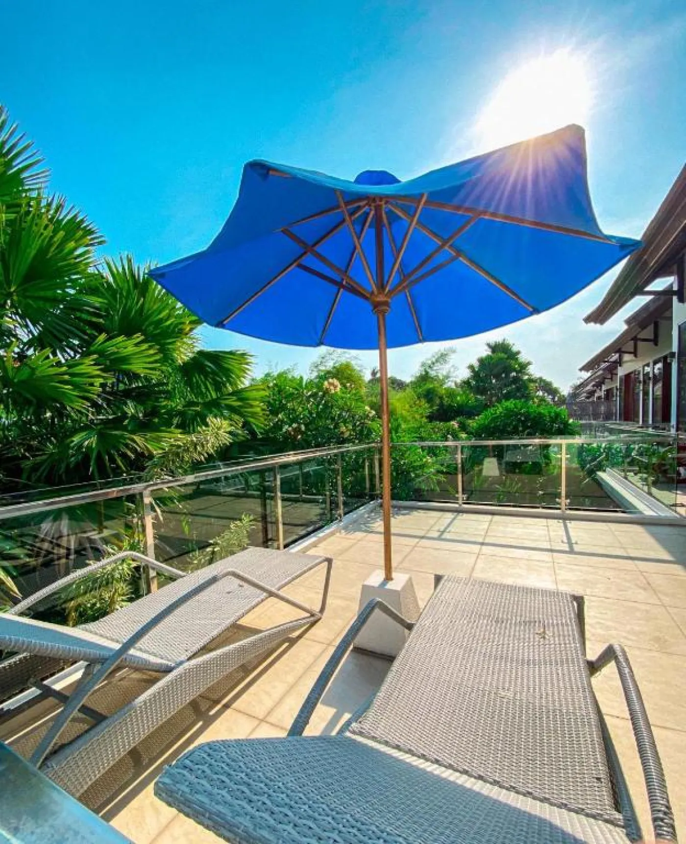 Bright Balinese dining area with wooden table and chairs, framed Hindu goddess artwork, potted plants, and open kitchen under warm ceiling lights. - Bali Villas