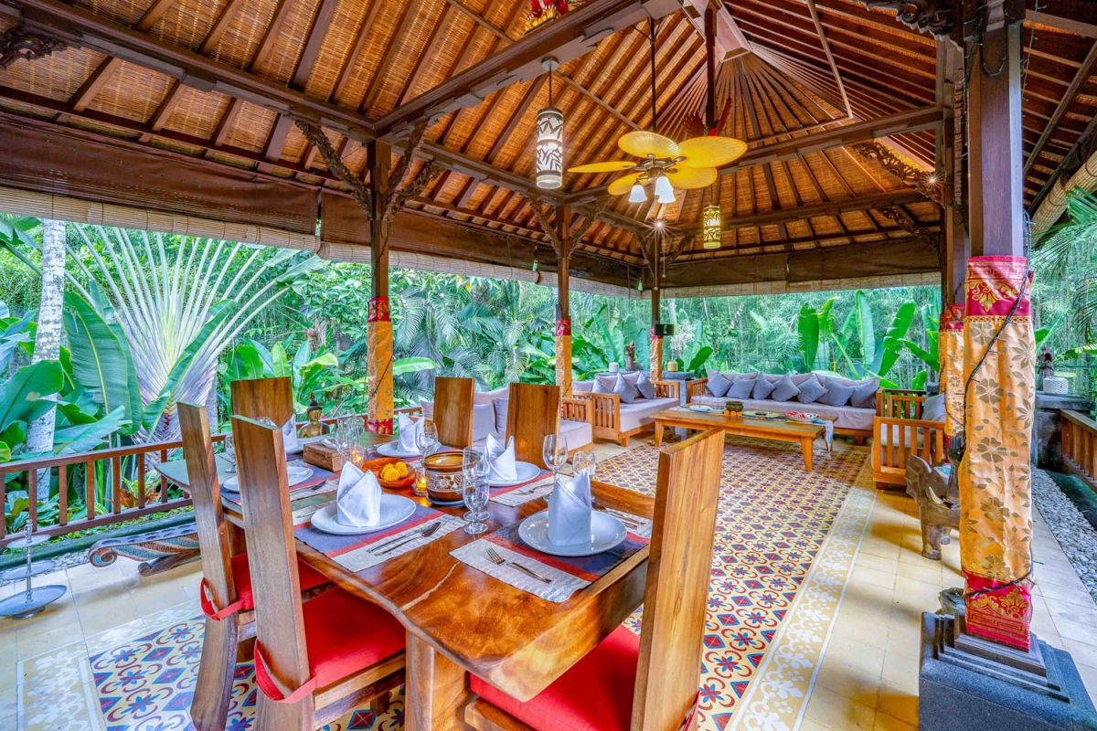 Modern tropical kitchen interior with black granite countertop, wooden cabinets, fresh pineapple and dragon fruit bowl, potted plants, and lush palm view through window. - Bali Villas