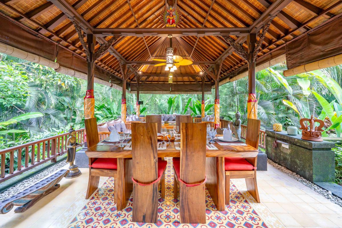 Modern tropical kitchen interior with black granite countertop, wooden cabinets, fresh pineapple and dragon fruit bowl, potted plants, and lush palm view through window. - Bali Villas