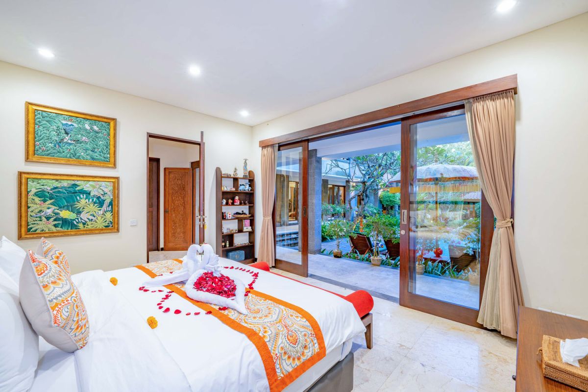 Modern tropical kitchen interior with black granite countertop, wooden cabinets, fresh pineapple and dragon fruit bowl, potted plants, and lush palm view through window. - Bali Villas