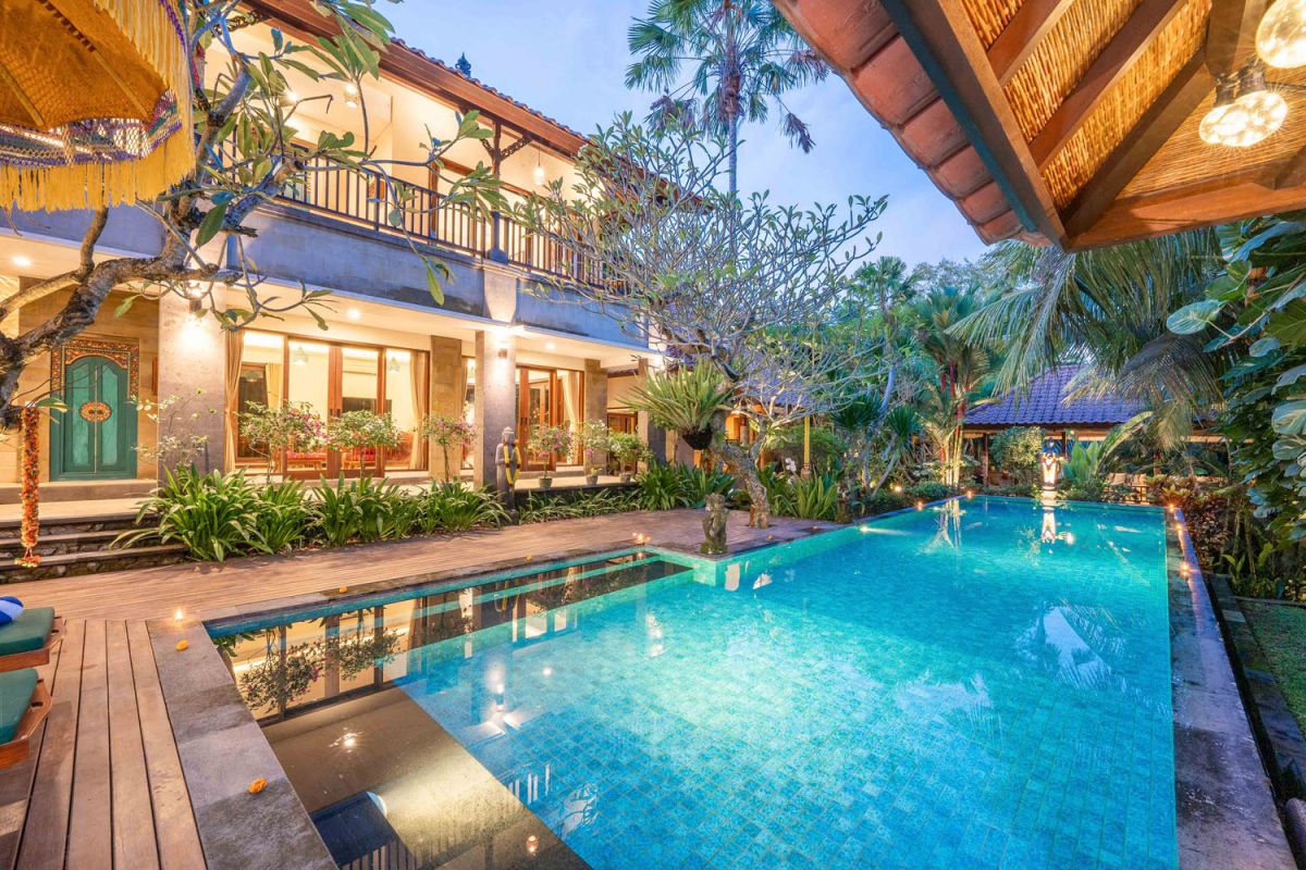 Modern tropical kitchen interior with black granite countertop, wooden cabinets, fresh pineapple and dragon fruit bowl, potted plants, and lush palm view through window. - Bali Villas