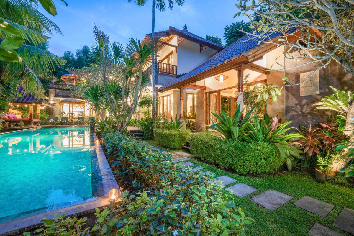 Modern tropical kitchen interior with black granite countertop, wooden cabinets, fresh pineapple and dragon fruit bowl, potted plants, and lush palm view through window. - Bali Villas