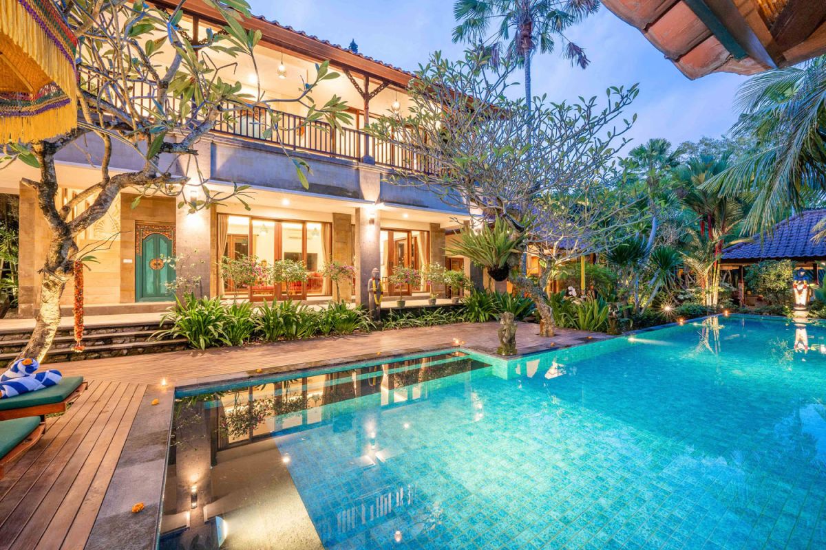 Modern tropical kitchen interior with black granite countertop, wooden cabinets, fresh pineapple and dragon fruit bowl, potted plants, and lush palm view through window. - Bali Villas