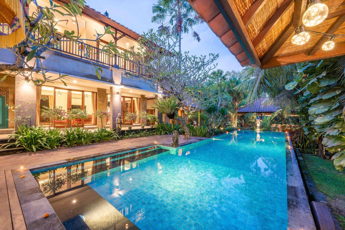 Modern tropical kitchen interior with black granite countertop, wooden cabinets, fresh pineapple and dragon fruit bowl, potted plants, and lush palm view through window. - Bali Villas