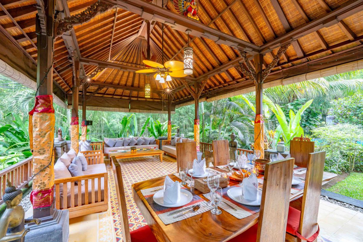 Modern tropical kitchen interior with black granite countertop, wooden cabinets, fresh pineapple and dragon fruit bowl, potted plants, and lush palm view through window. - Bali Villas