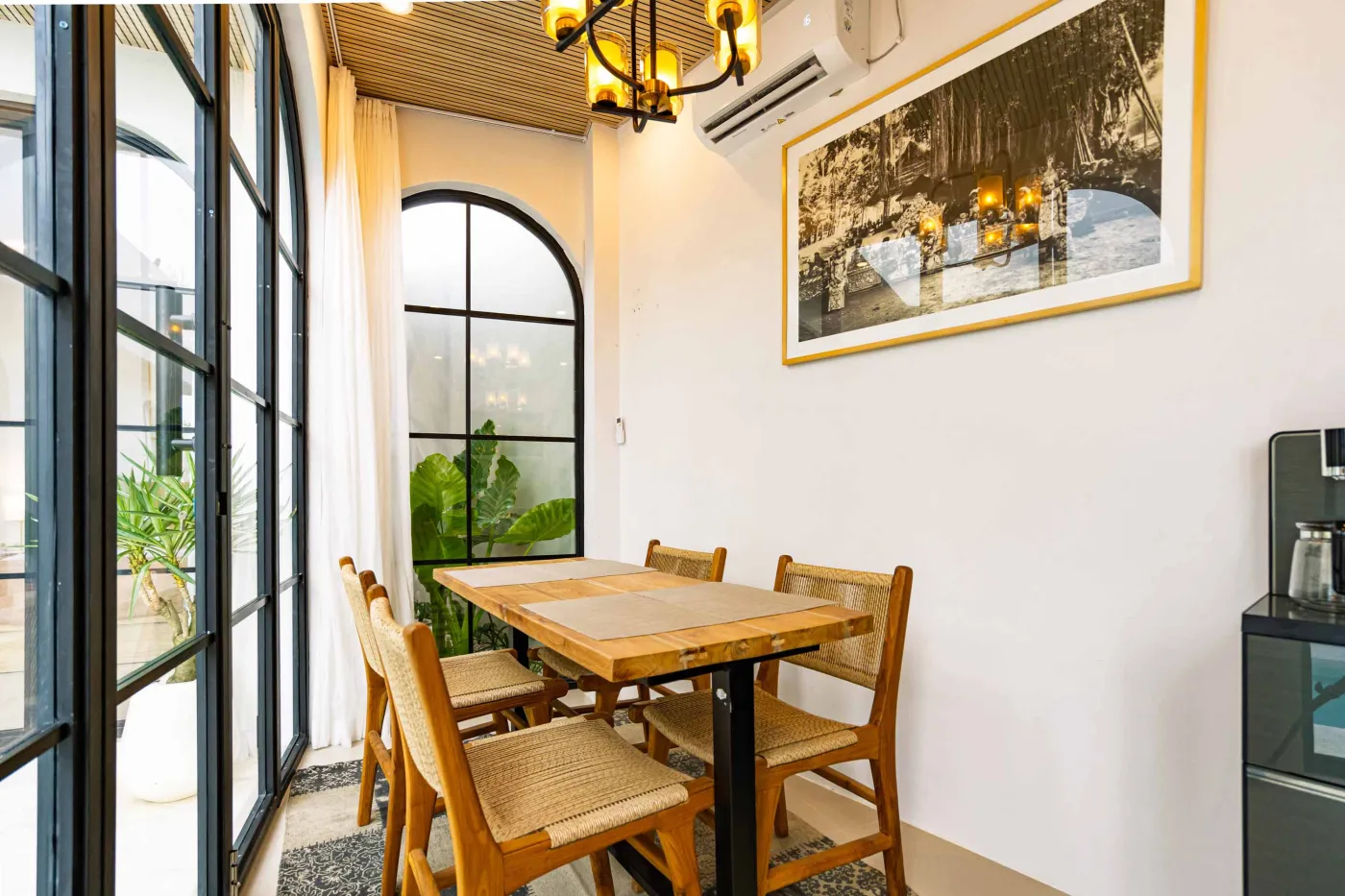 Luxurious modern bathroom with textured stone walls, arched black-framed windows overlooking tropical palms, freestanding white bathtub filled with red petals, and sleek vanity sink. - Bali Villas