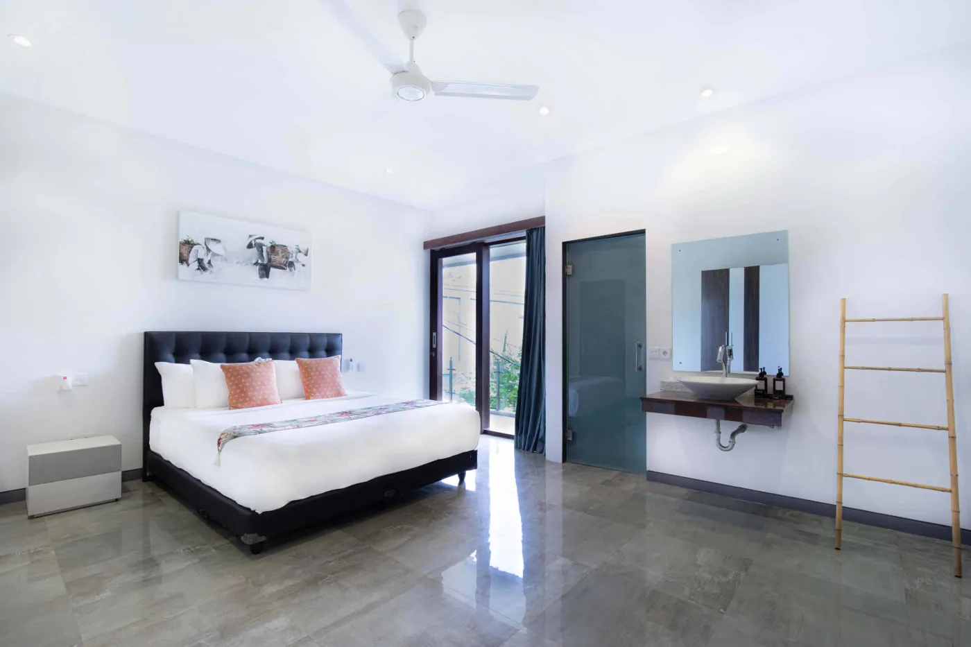 Modern black-tiled bathroom with freestanding white bathtub, handheld shower, and folded towels on rack. - Bali Villas