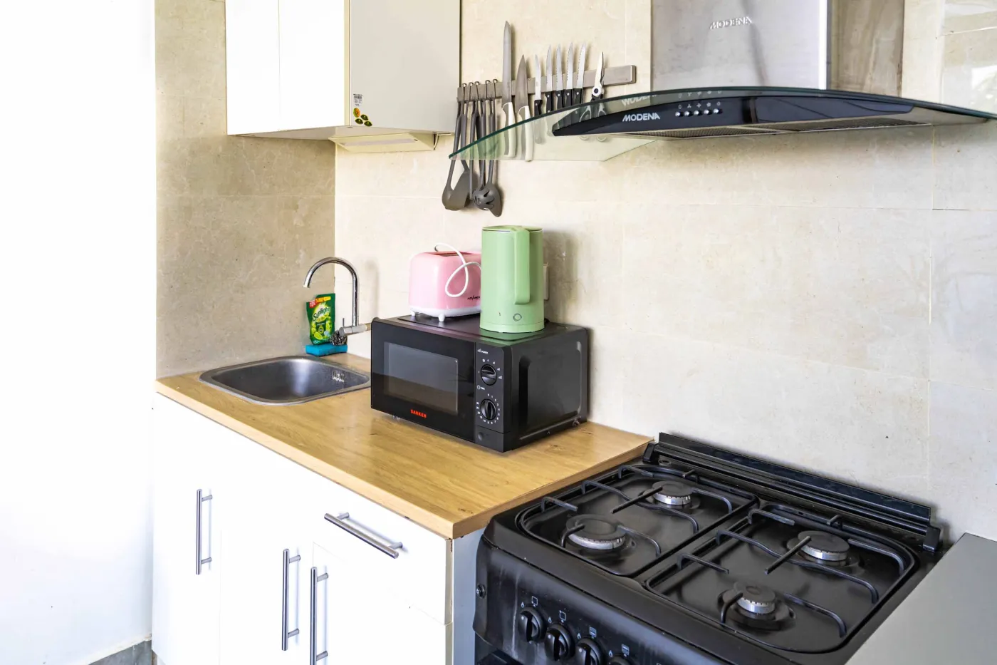 Cozy modern living room with green velvet sofa, wooden coffee table, potted plant, and adjacent white kitchen. - Bali Villas