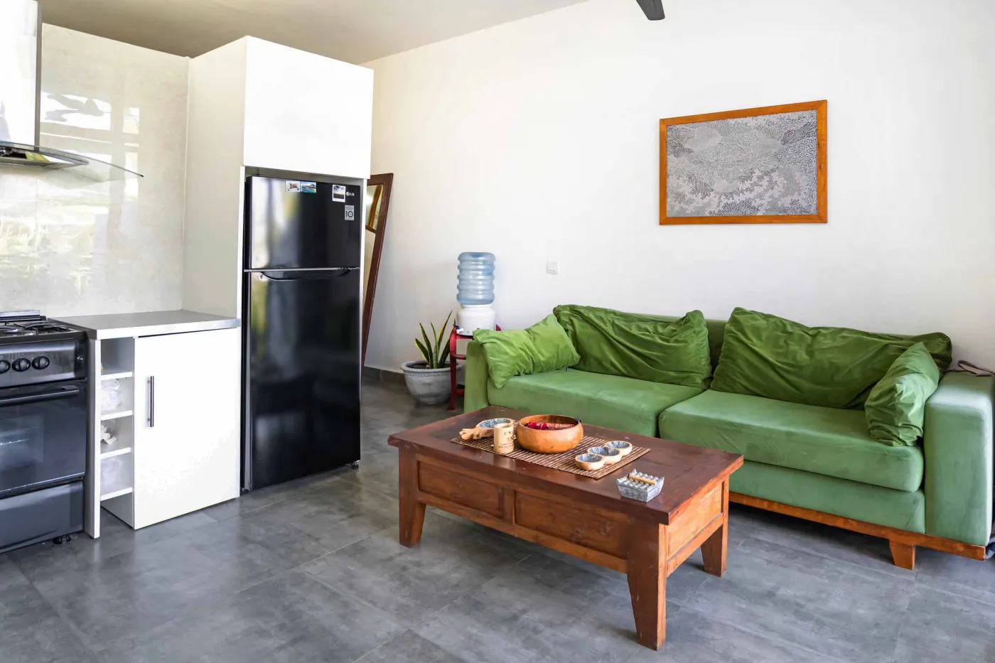 Cozy modern living room with green velvet sofa, wooden coffee table, potted plant, and adjacent white kitchen. - Bali Villas