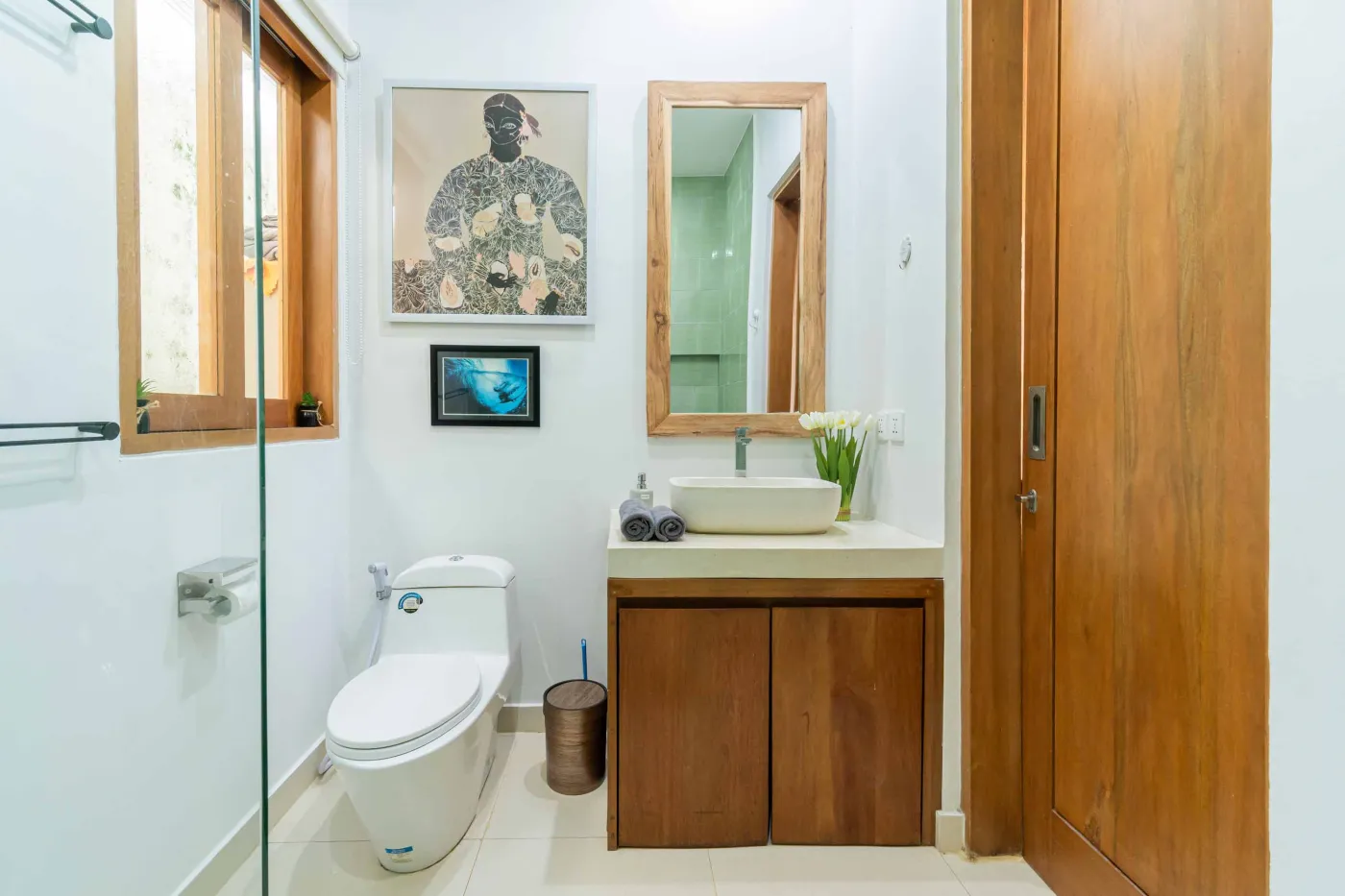 Modern minimalist interior with wooden desk, potted cactus in round window, rattan lamp, and tiled flooring. - Bali Villas