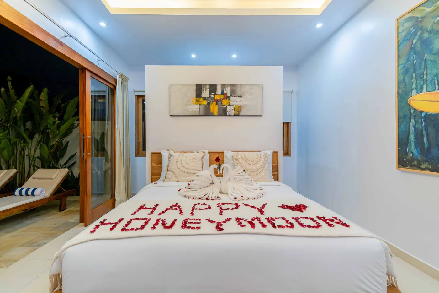 Bright modern Balinese kitchen with white countertops, wooden cabinets, potted plants, large windows, and a wall-mounted TV. - Bali Villas
