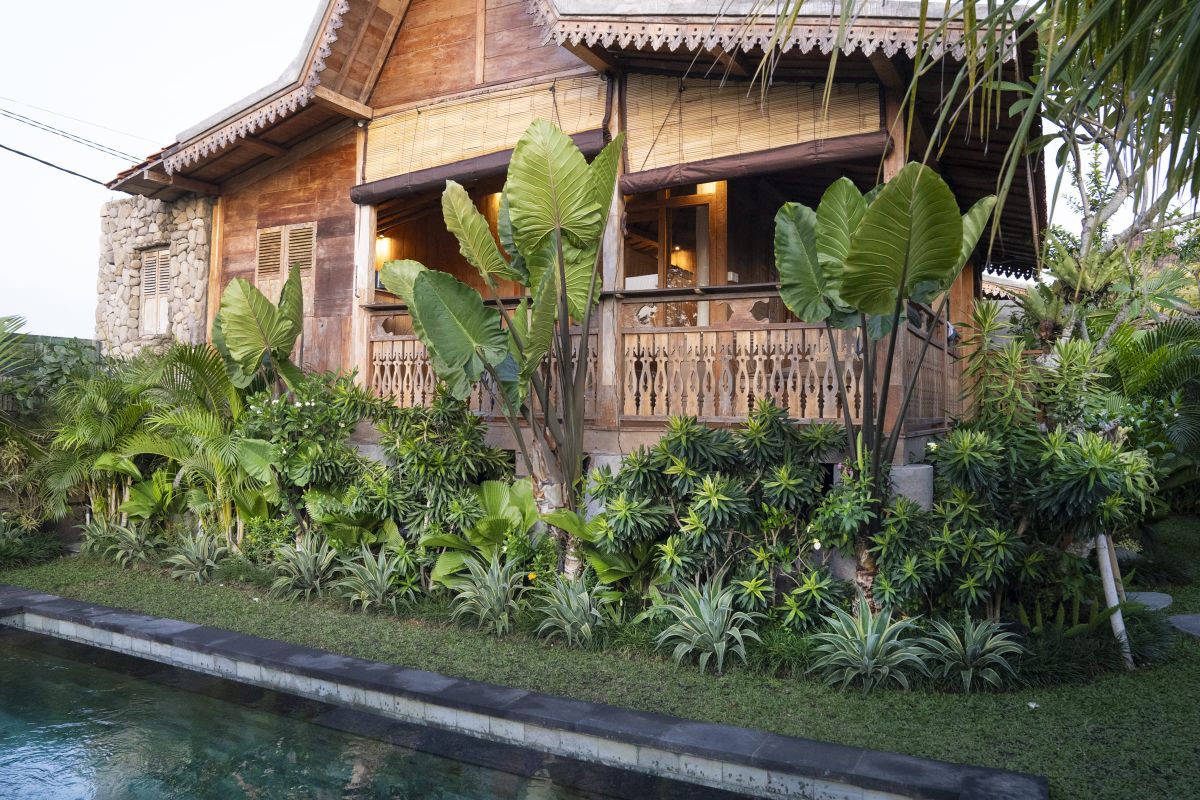 Rustic Balinese bathroom with wooden vanity, double sinks, orchid plant, towels, and pebble stone wall. - Bali Villas