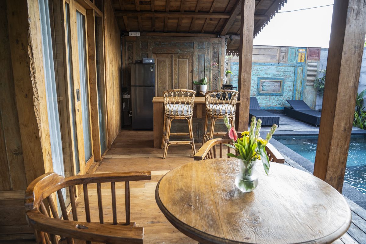 Rustic Balinese bathroom with wooden vanity, double sinks, orchid plant, towels, and pebble stone wall. - Bali Villas