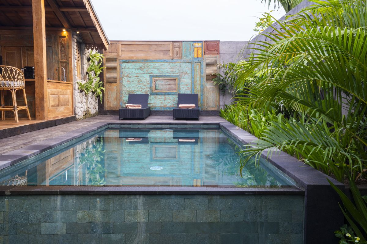Rustic Balinese bathroom with wooden vanity, double sinks, orchid plant, towels, and pebble stone wall. - Bali Villas