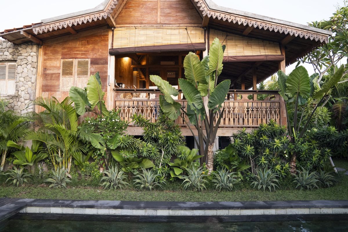 Rustic Balinese bathroom with wooden vanity, double sinks, orchid plant, towels, and pebble stone wall. - Bali Villas