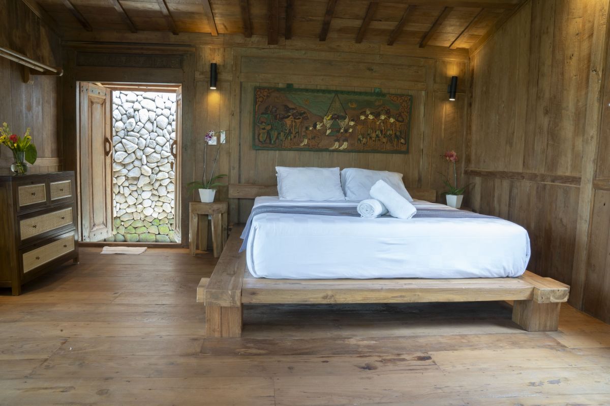 Rustic Balinese bathroom with wooden vanity, double sinks, orchid plant, towels, and pebble stone wall. - Bali Villas