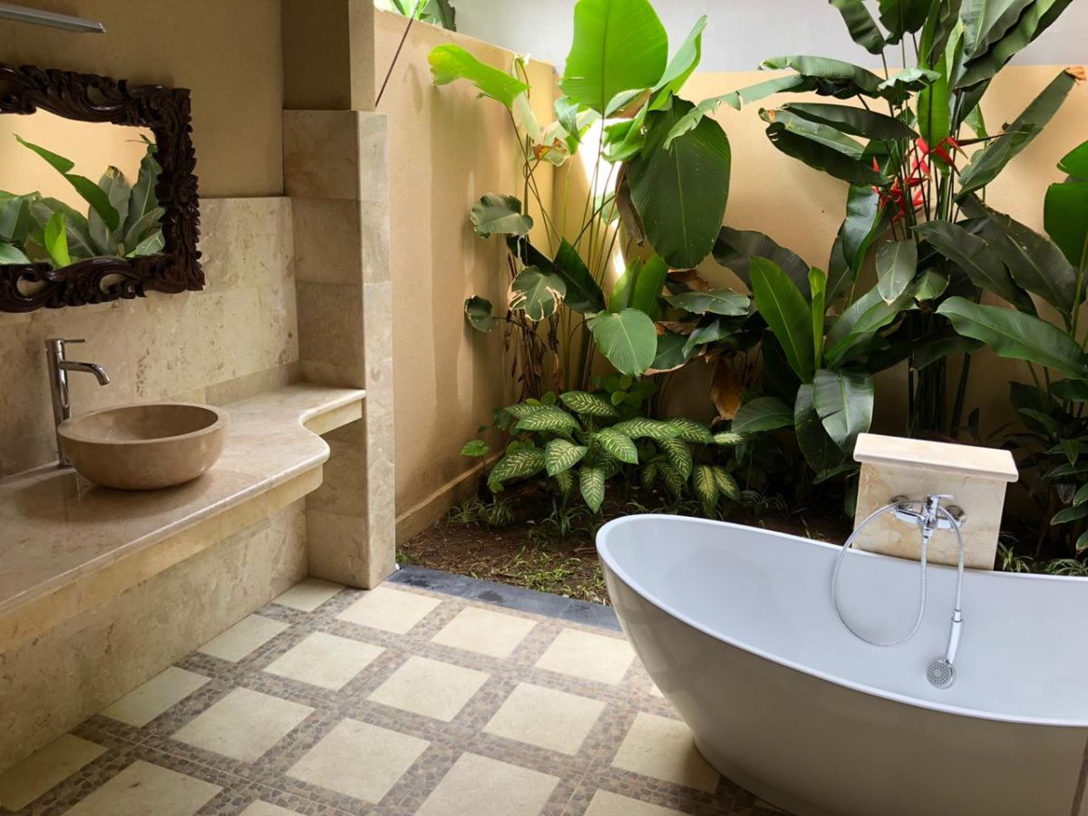 Serene tropical bathroom with stone sink, freestanding white bathtub, and lush green plants. - Bali Villas