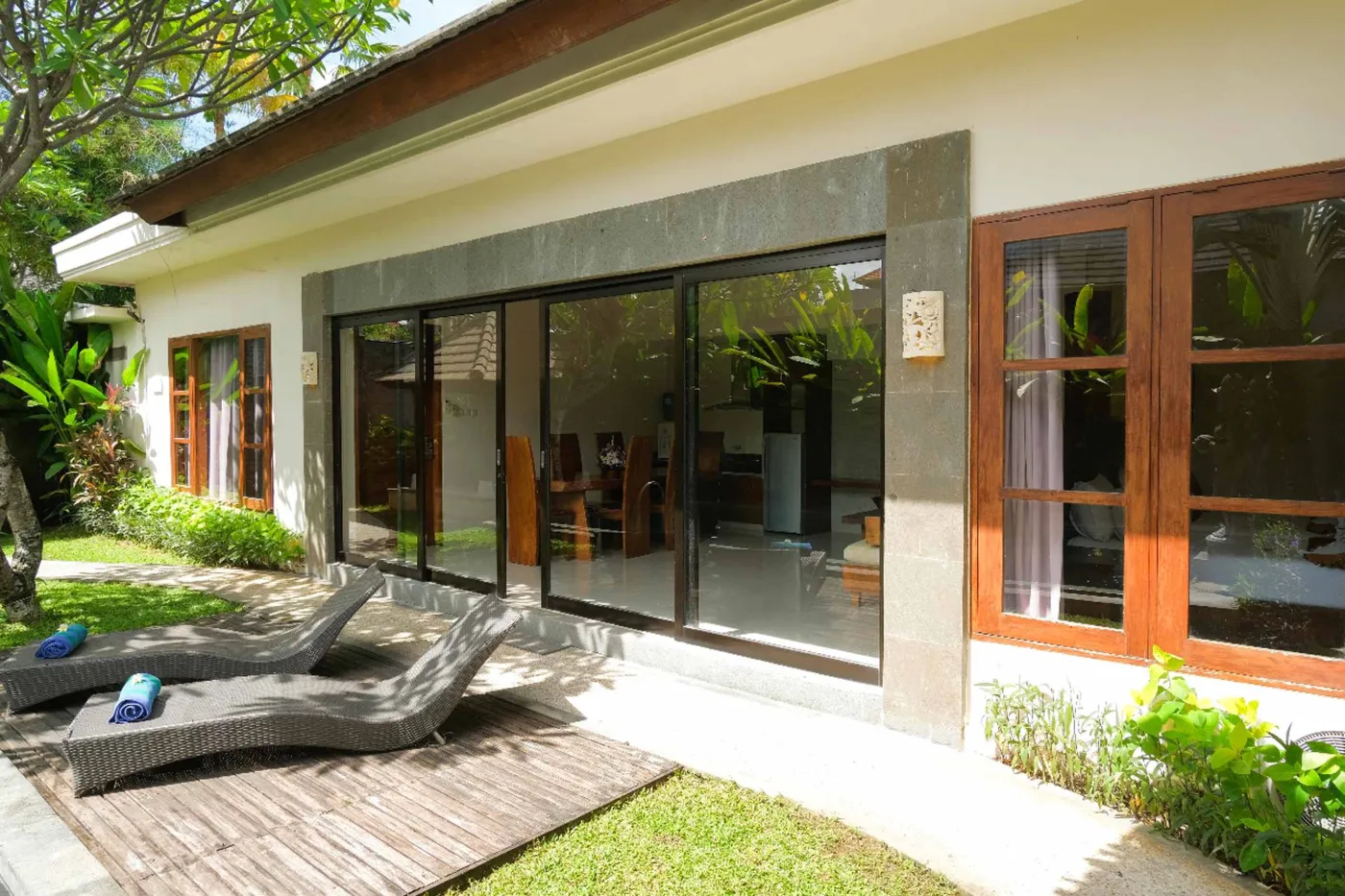 Modern luxury hotel bathroom with wooden vanity, white sink, stone wall, glass shower enclosure, freestanding bathtub, and folded towels. - Bali Villas
