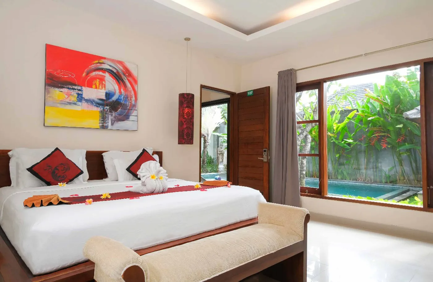 Modern luxury hotel bathroom with wooden vanity, white sink, stone wall, glass shower enclosure, freestanding bathtub, and folded towels. - Bali Villas