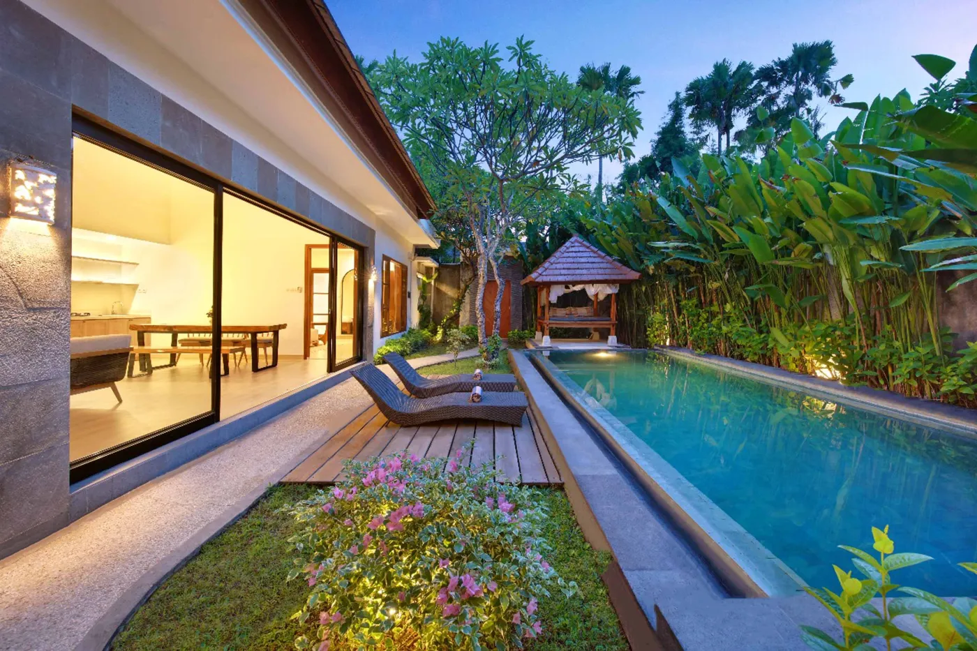 Spacious Balinese-style hotel bedroom with twin wooden platform beds, abstract colorful wall art, mirrored wardrobe, and arched bathroom doorway. - Bali Villas