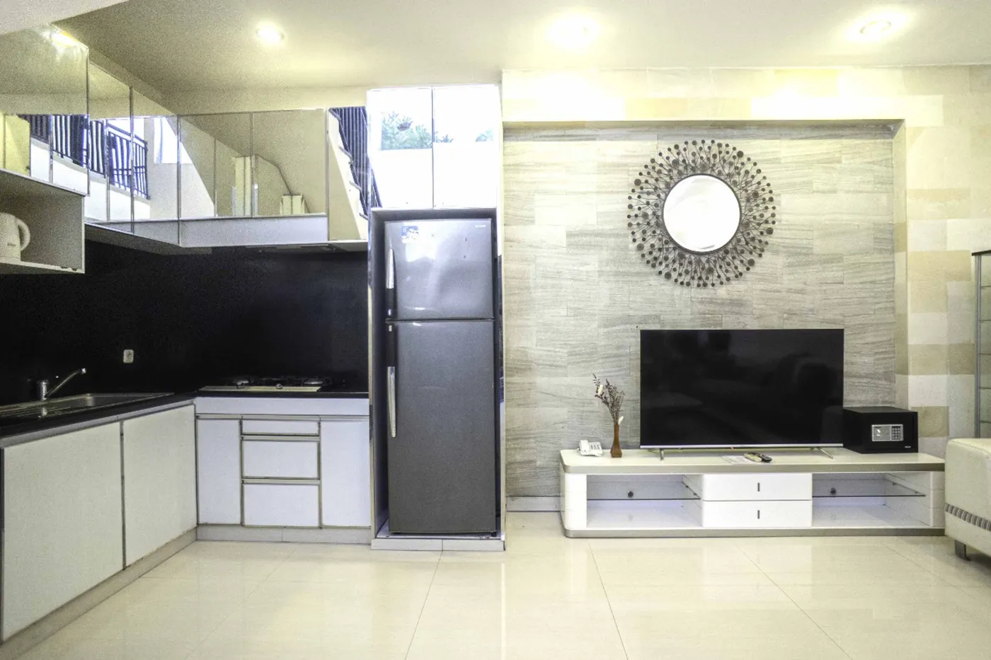 Modern luxury bathroom with freestanding bathtub, wooden vanity sink, gold-framed mirror, stone accent wall, and white marble tiles. - Bali Villas